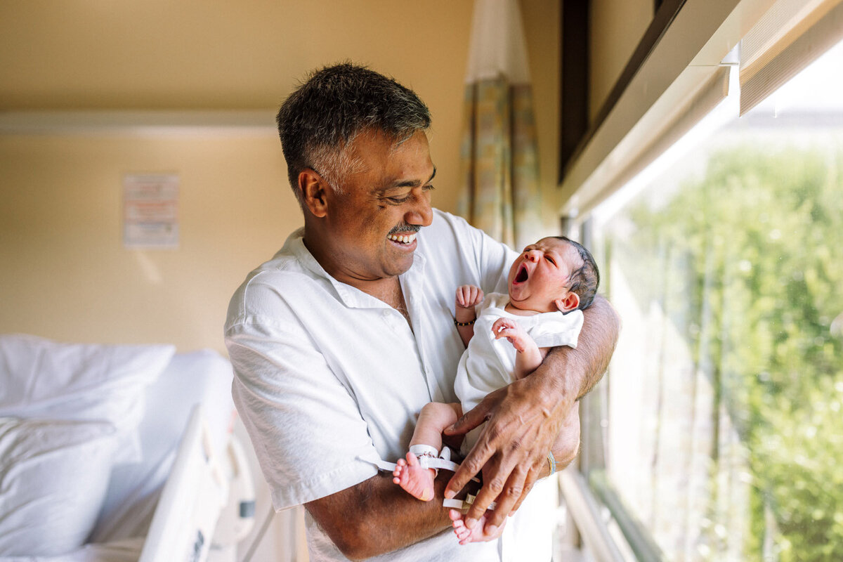 grandfather holding and smiling at yawning newborn in hospital