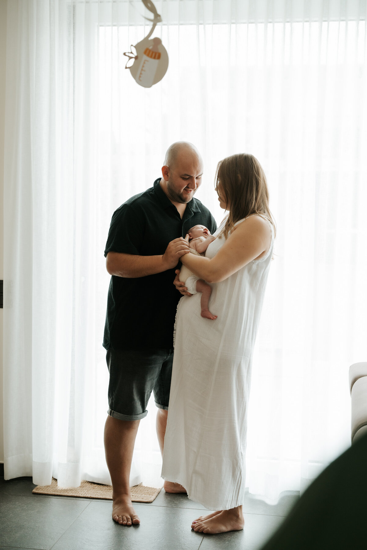 Mama en papa kijken lachend toe naar hun baby tijdens de newbornshoot aan huis