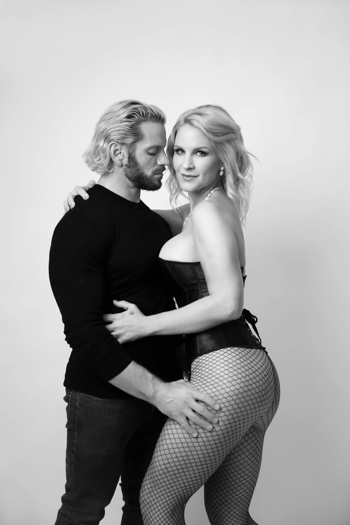 a couple hugging each other. The man is wearing a black sweater and black jeans. The woman is wearing a black corset