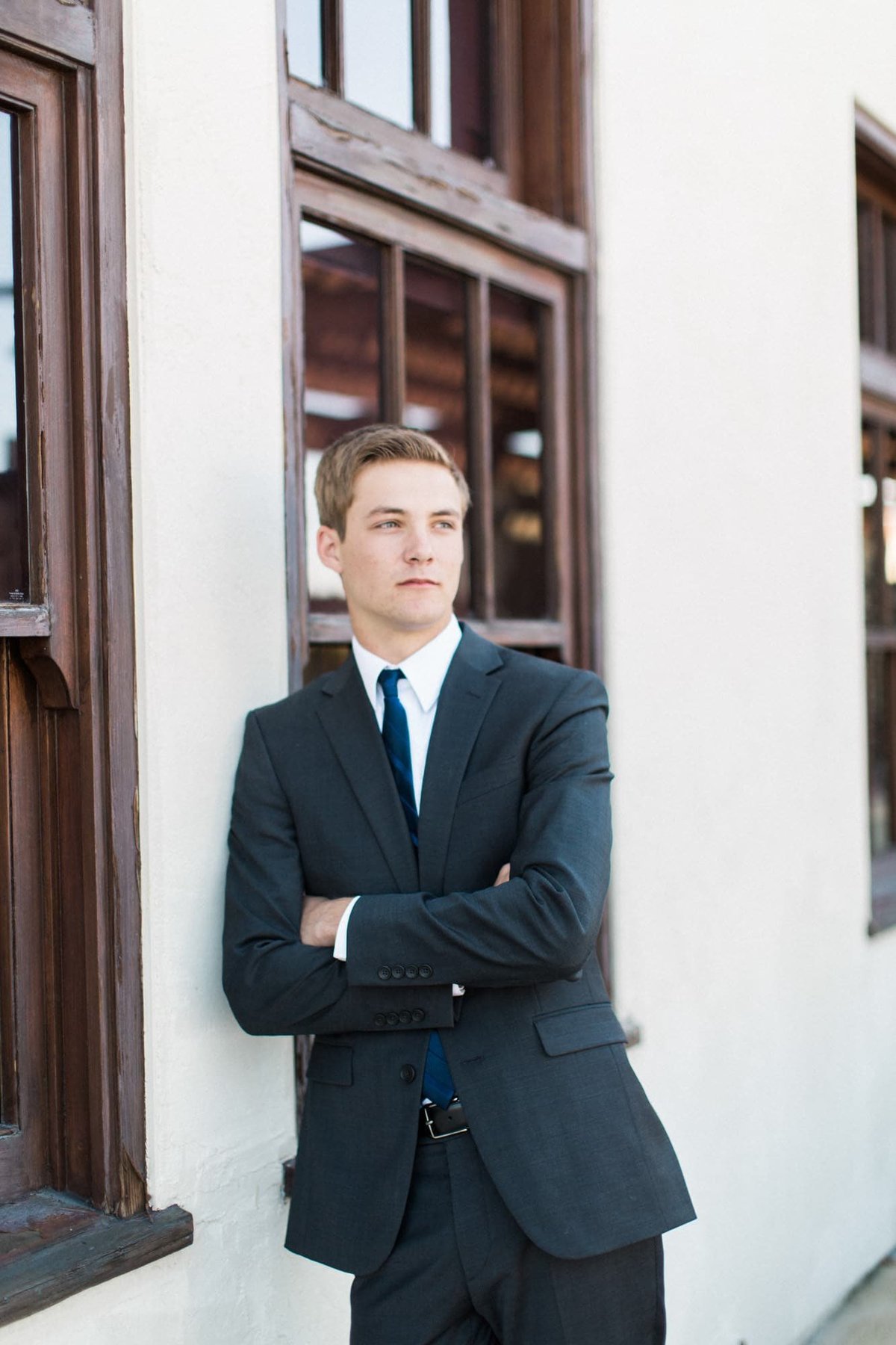 Young man dressed in a suit leans against a wall during his senior portrait photo session