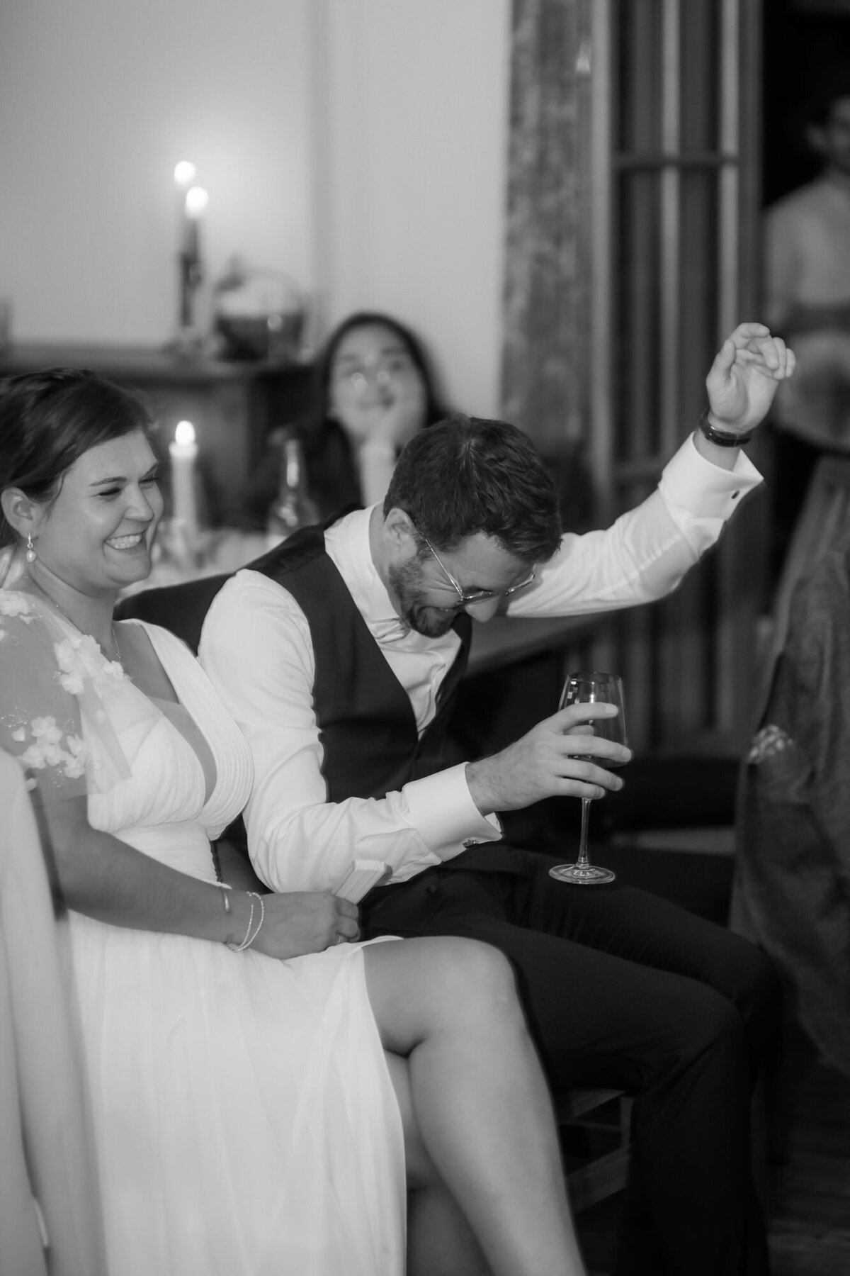 Der Bräutigam jubelt bei der Feier, während das Hochzeitspaar nebeneinander sitzt.