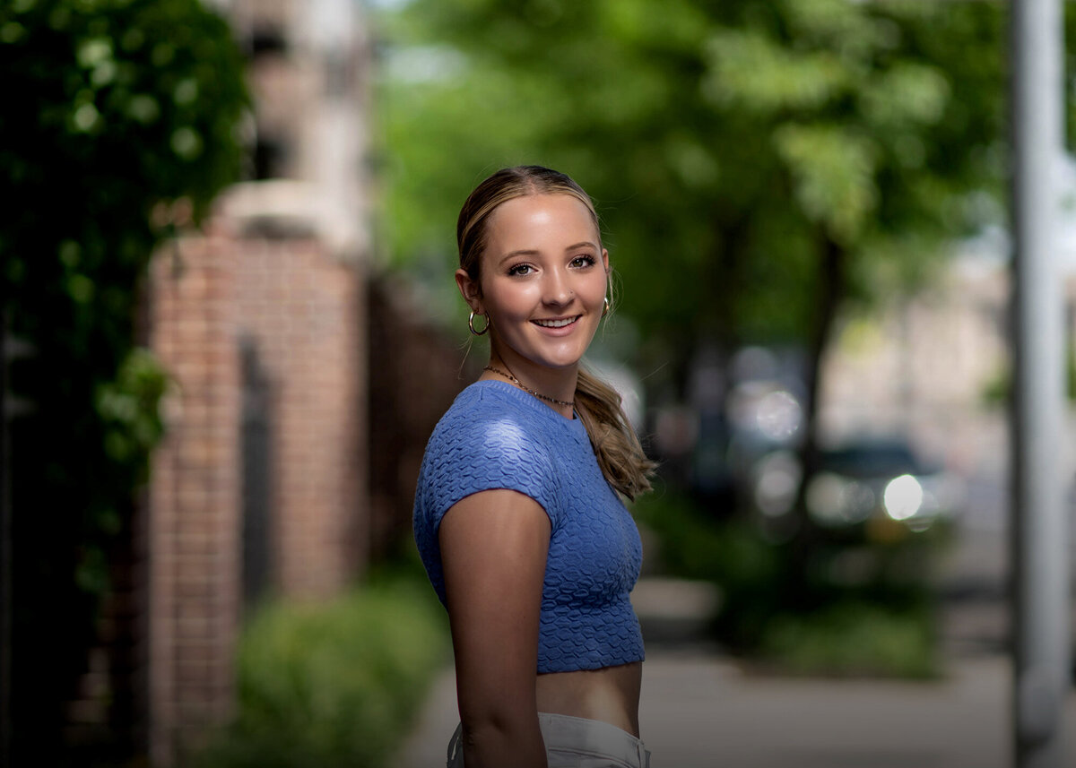 A woman smiles over her shoulder while walking the sidewalk in a blue top