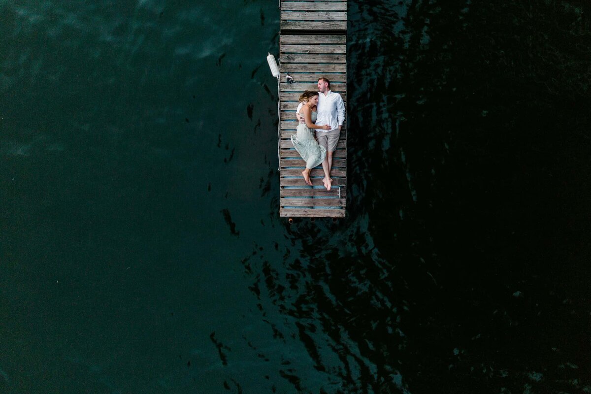 Drone photo of a couple laying on a dock surrounded by deep teal water