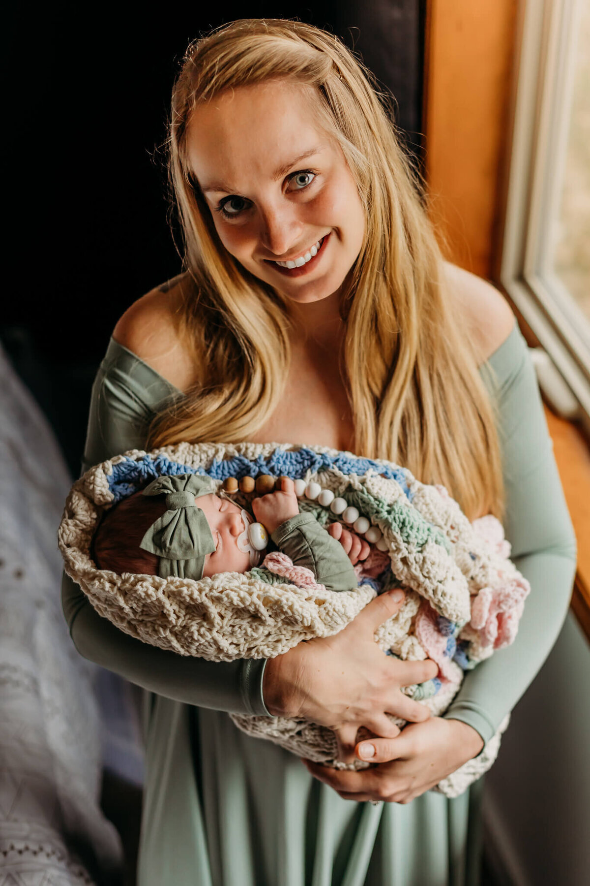 mom in green dress holding baby wrapped in heirloom blanket
