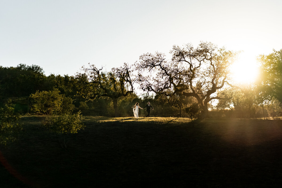 Groom and Bride stroll down between shrub greenery and trees in Malibu for a wedding photo session, photo by Tanya Parada