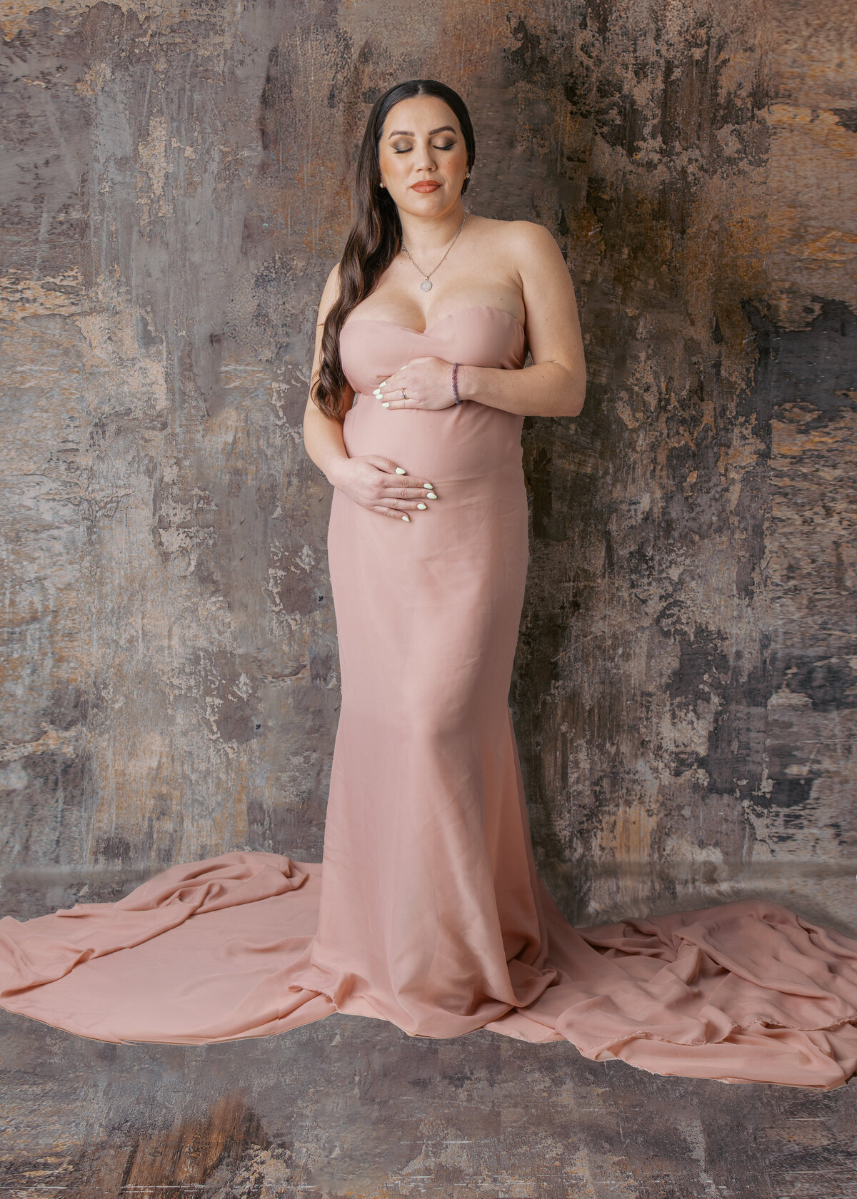 Expecting mother in elegant pink material in a softly lit studio, showcasing her baby bump with a serene expression in Waldwick, NJ.