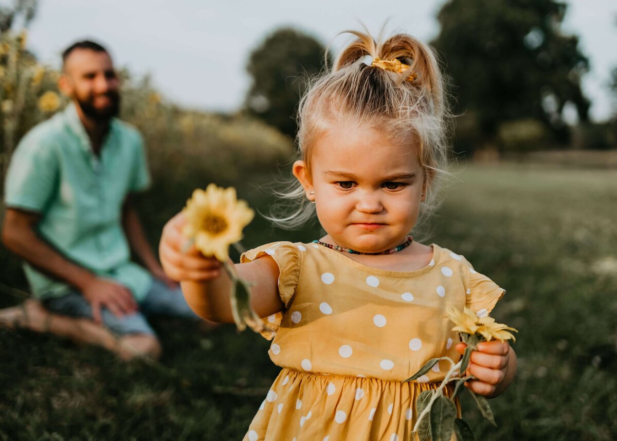 A little girl is holding a flower in front of her father, captured by a Pittsburgh family photographer.