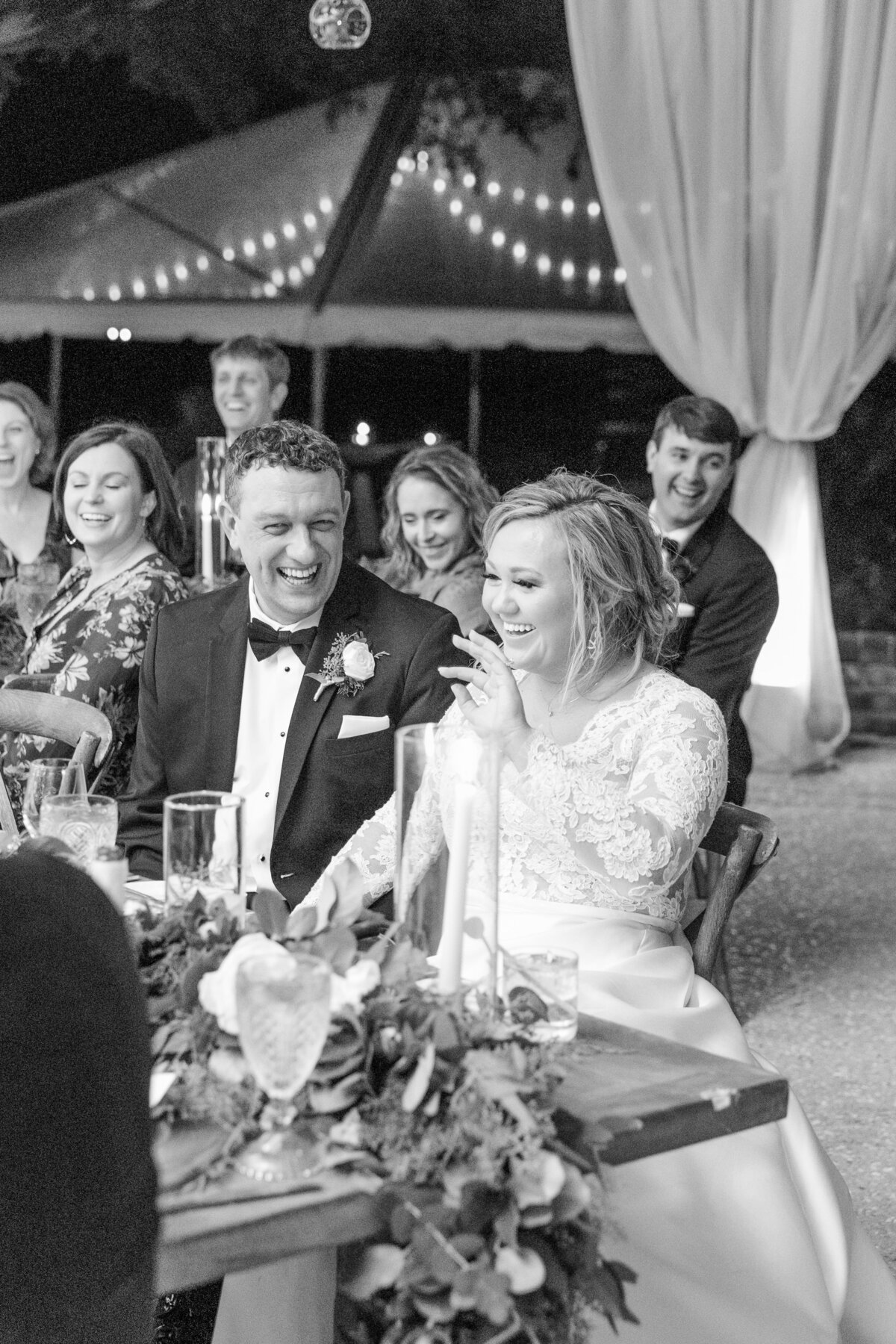 Candid photo of bride and groom laughing during toasts at their wedding in Charleston photographed by Charleston wedding photographer Dana Cubbage.