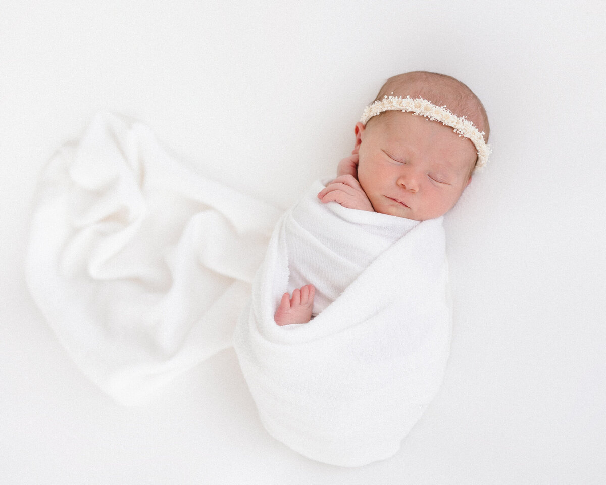 Sleeping newborn baby girl wrapped in a white swaddle by Missy Marshall photography