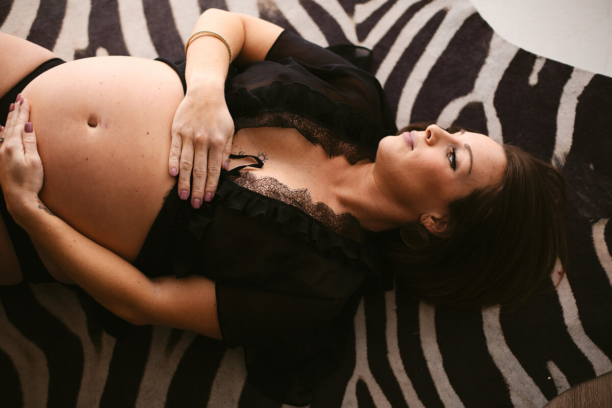 A beautiful pregnant momma lays seductively on a zebra rug in a Bentonville boudoir studio.