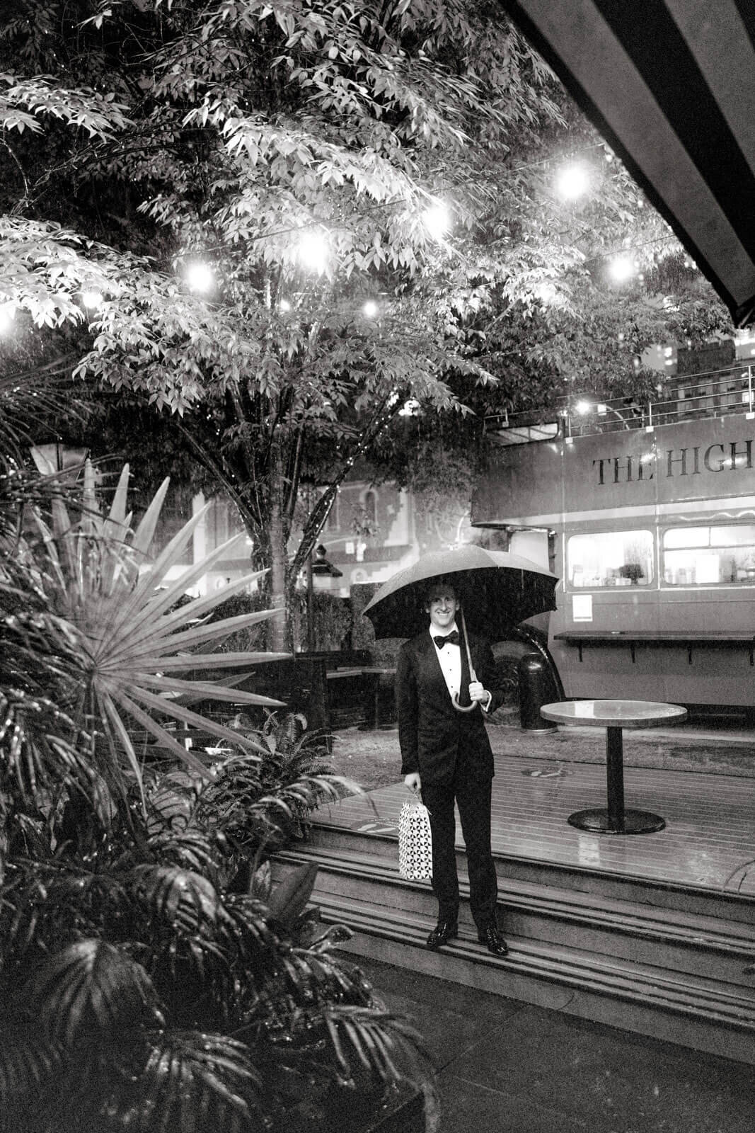 The groom is holding an umbrella in the outdoor dining area while raining, at The High Line Hotel Chelsea, NYC. Image by Jenny Fu Studio