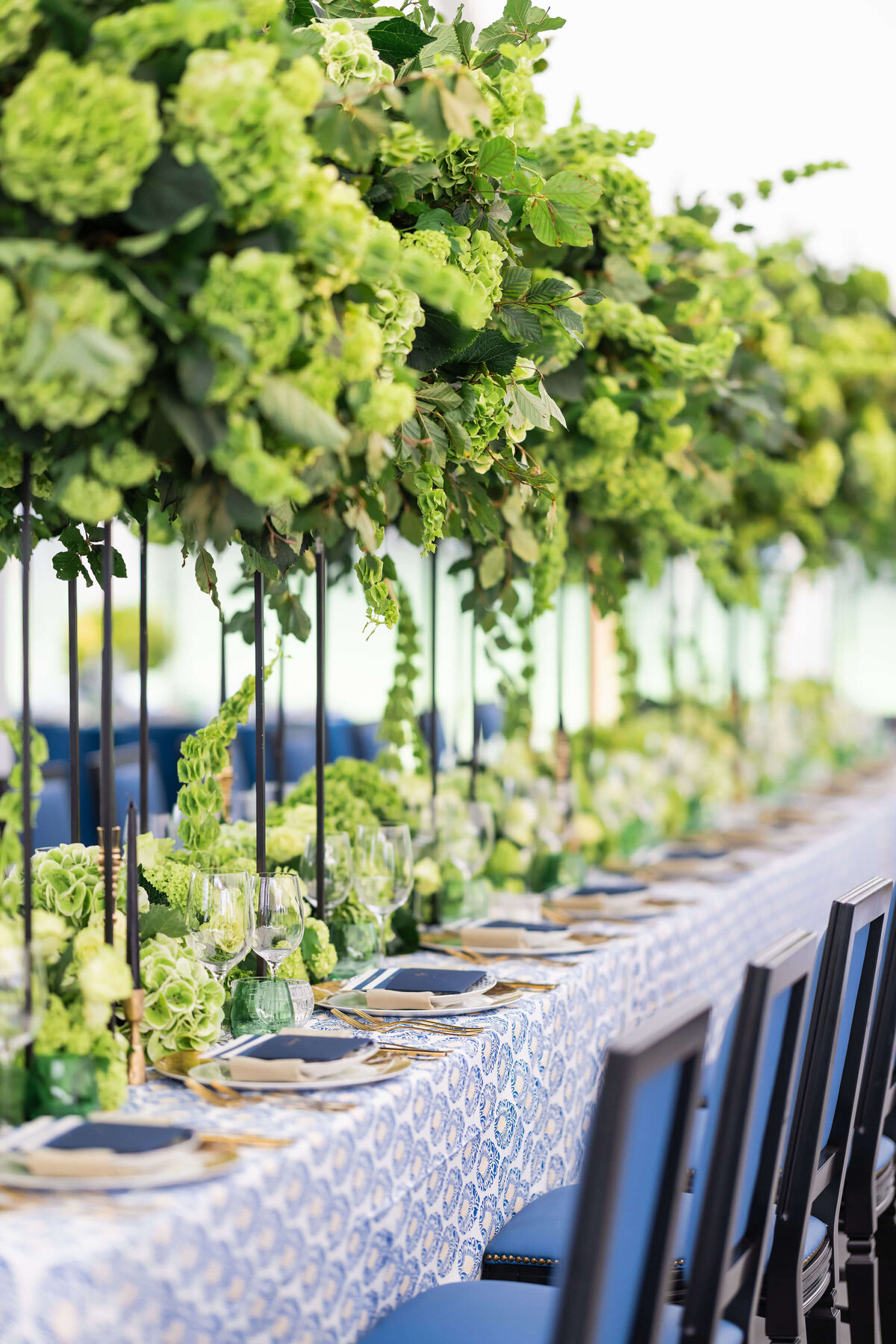long dinner table for a birthday party with tall and low lime green floral arrangements along the centre of the table which is laid with blue patterned linen