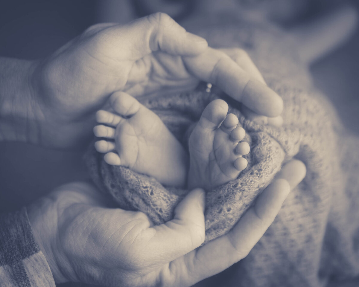 Detail image from a Pella Newborn Photographer of a father holding the feet of his newborn