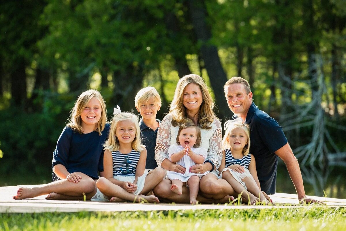 Parents sitting on a blanket on the grass with five kids.