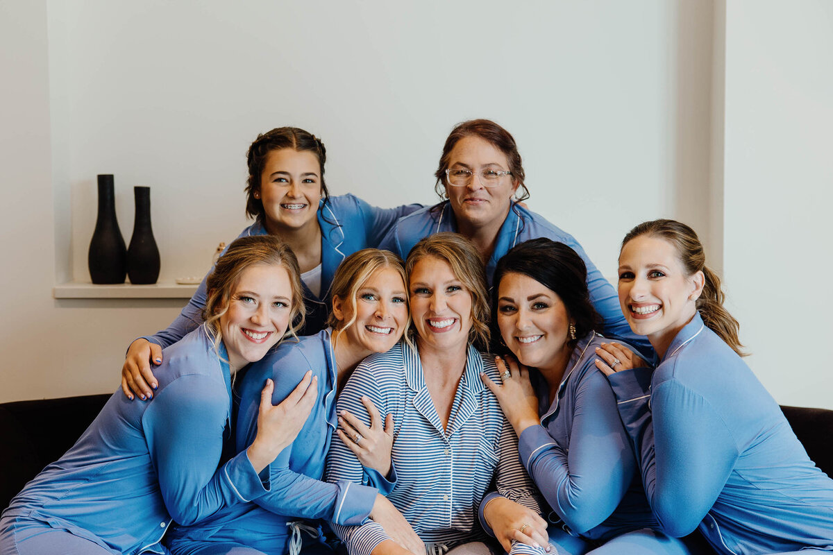 A wedding party sitting with a bride in matching pajamas smiling