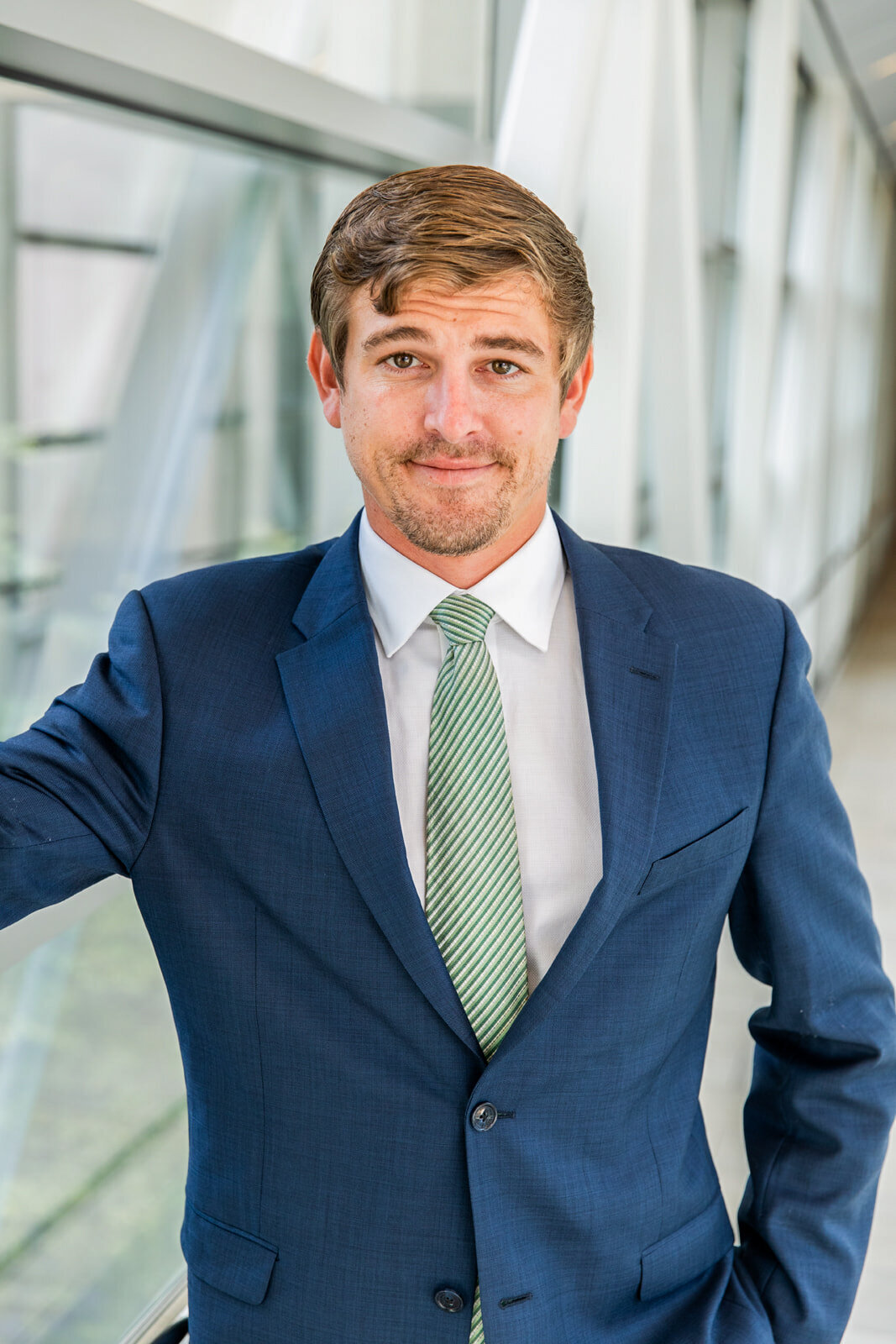 man wearing blue suit and green tie one hand in the pocket in front of a urban clear color background