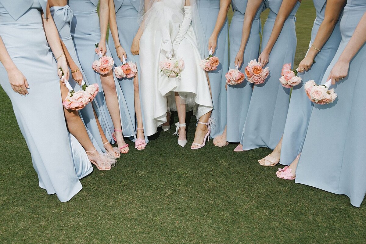 bride and brides' in a semi circle  holding bouquets and showing off their shoes