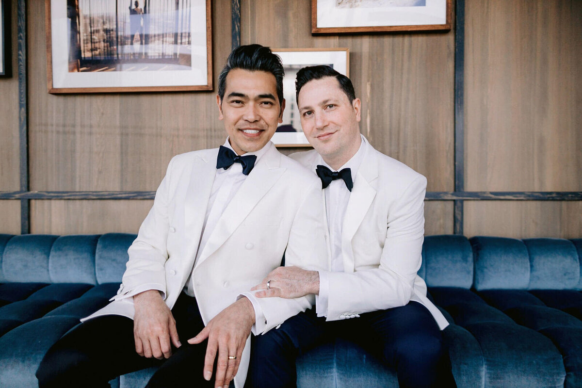 Two grooms wearing white suits are smiling in The Skylark, New York. Wedding Image by Jenny Fu Studio