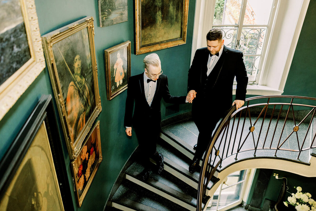 two grooms holding hands and walking down the stairs at the Manor of Greencrest Manor wedding