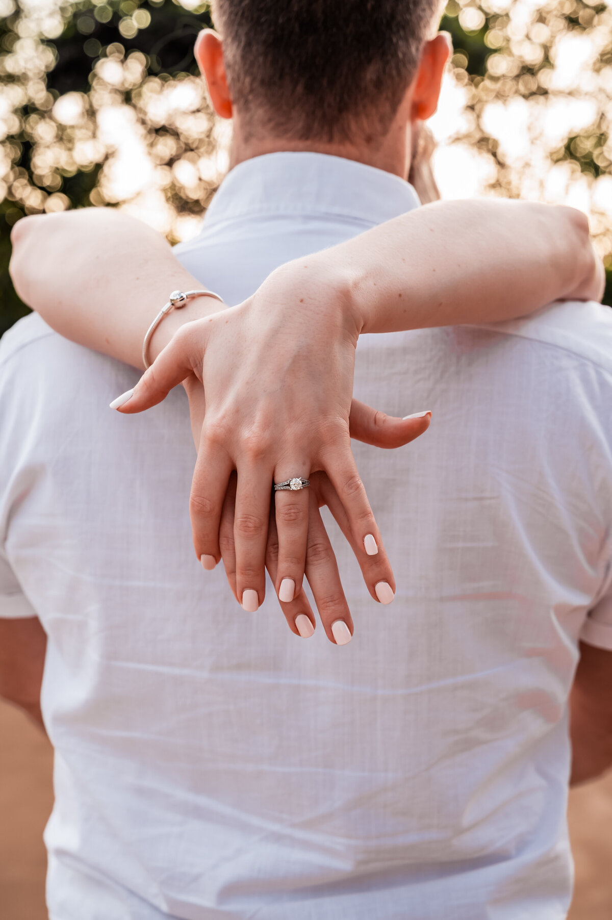 man with his back to the camera while holding his fiance as she sweeps her arms over his shoulders to show off her engagement ring - Townsville Engagement Photography by Jamie Simmons