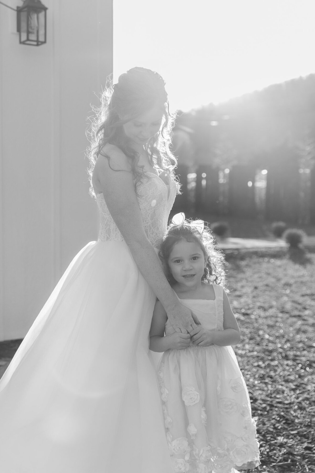 A bride holds her daughter close to her while holding her hand on her wedding day. The photo is in black and white.