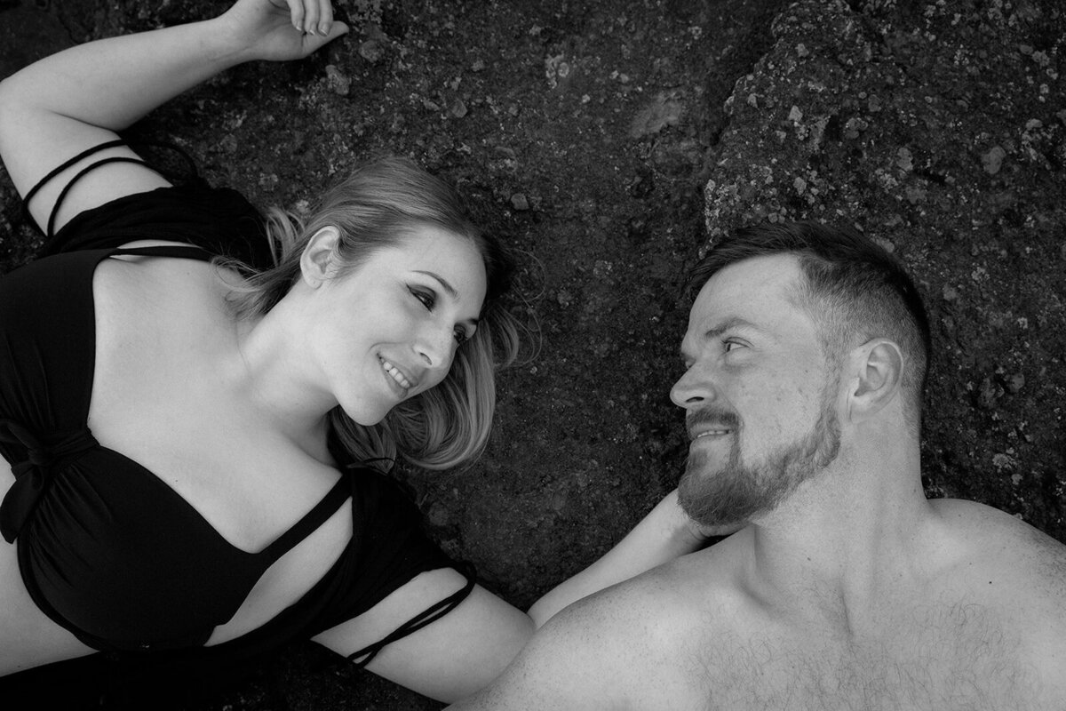 Two lovers stare at each other while lying on a beach.