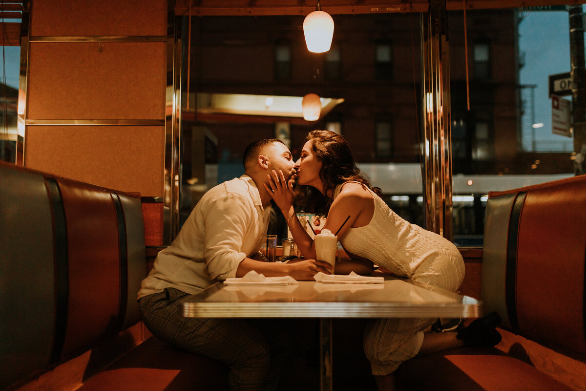 Couple kissing across the table in a diner booth