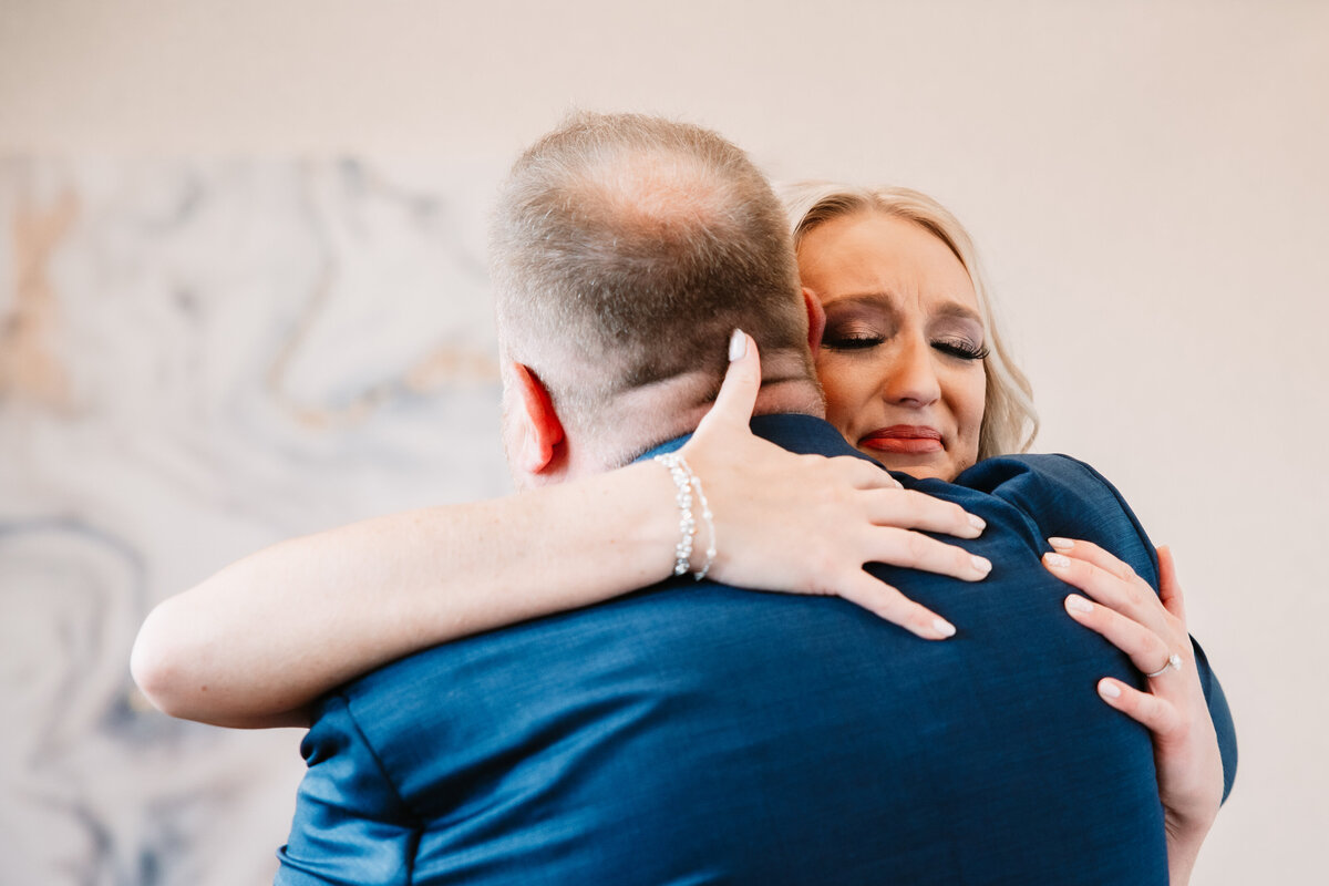 A bride has an emotional hug with her father in a blue suit