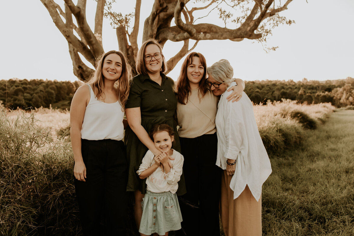 Three generations grandmother , daughter-in-law , daughter and granddaughter  at golden hour with a beautiful big tree