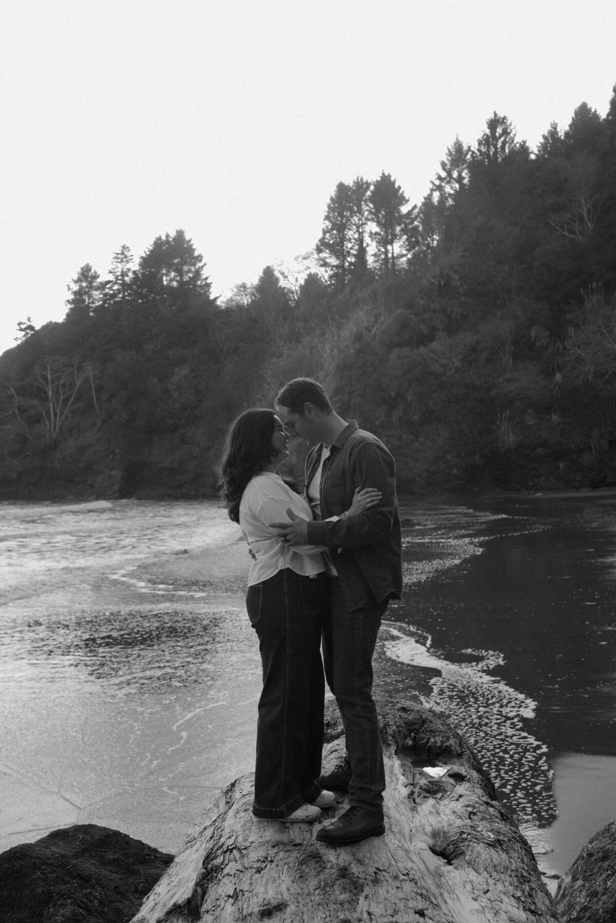 candid engagement portrait of couple wrapped in each other’s arms as the ocean breeze flows around them
