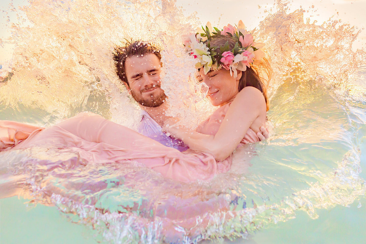 Candid water portrait of a woman wearing a floral crown and pink dress in the arms of her husband while honeymooning in Maui