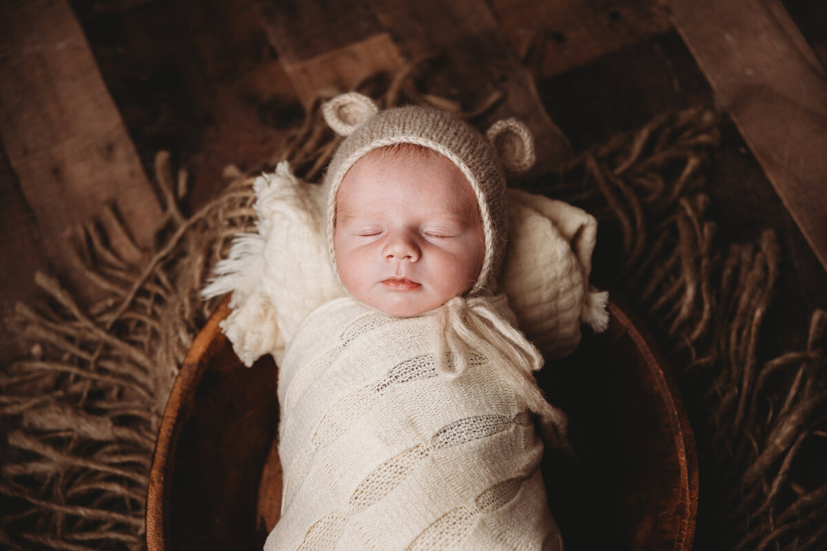 A baby laying in a basket with bear ears on.