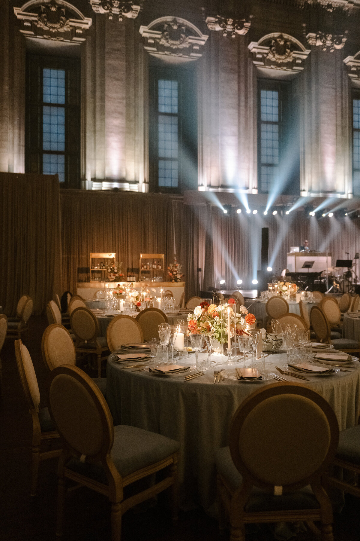 Tables at Theatre St James decorated with candles and garden floral centrepieces with spotlights lighting the background.