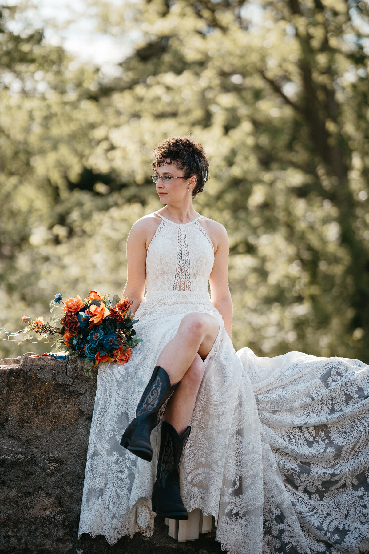 Bride sits on a stone wall with her legs crossed while looking into the distance