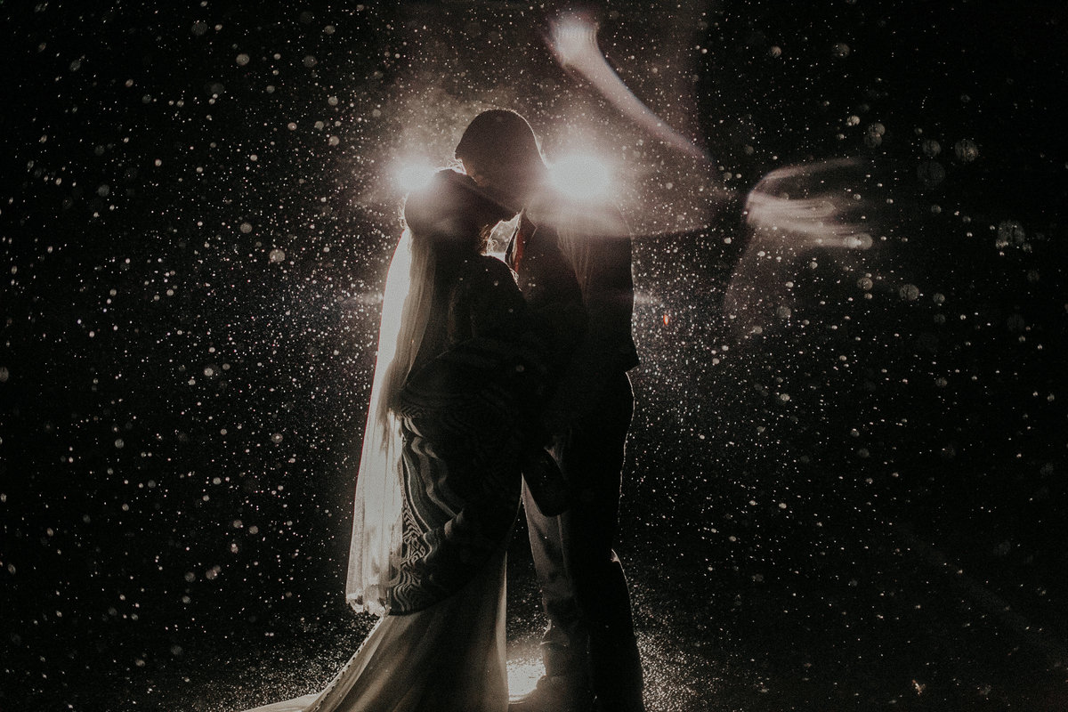 Couple kissing in car head lights in a rain storm during their elopement