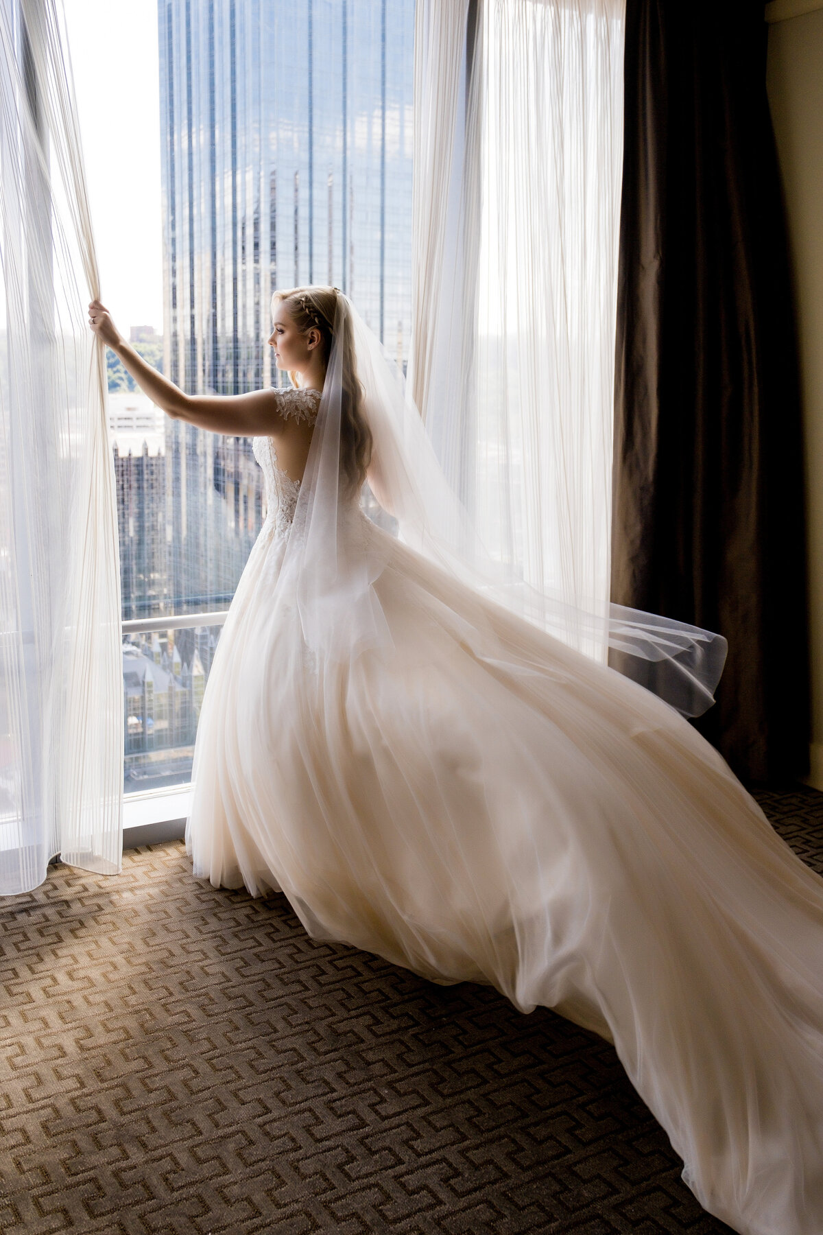 bride looking at the window at the fairmont hotel with wedding dress blowing behind her