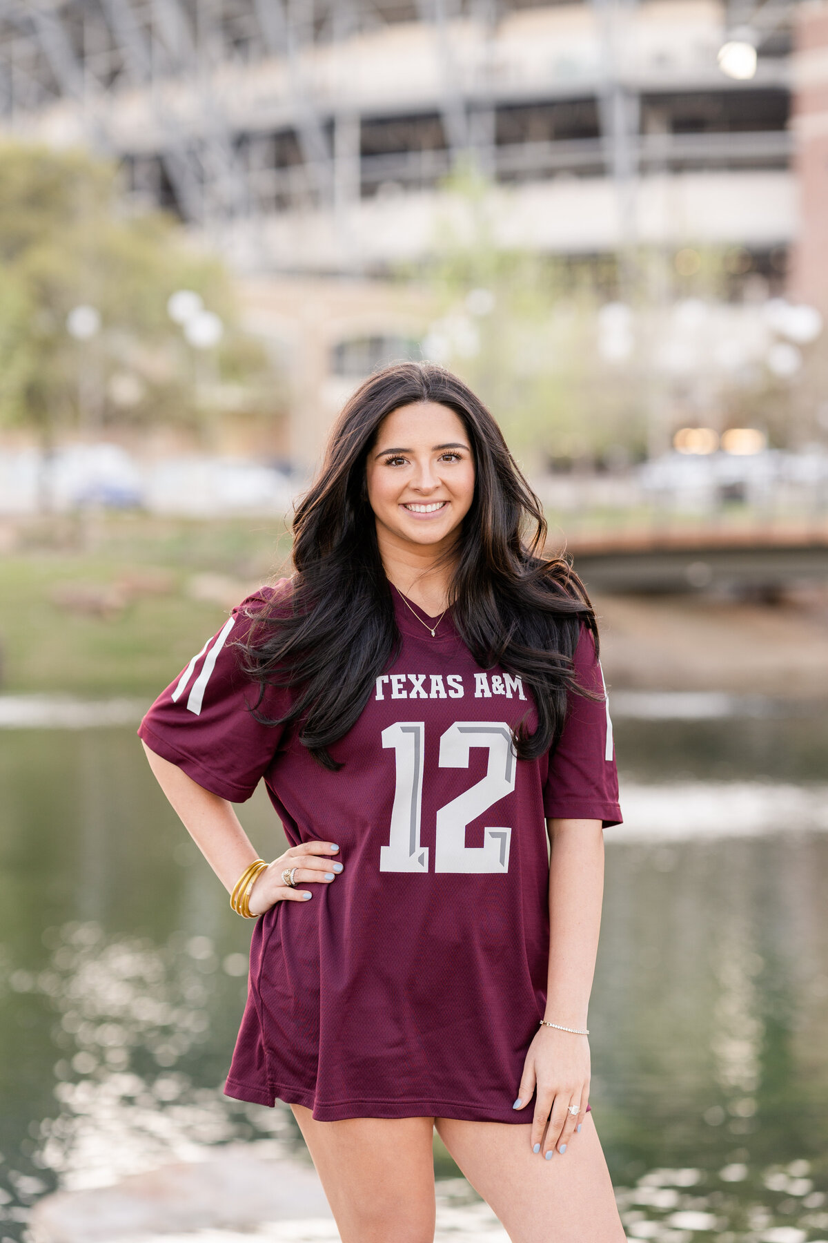 Texas A&M senior girl smiling with hand on hip and wearing maroon jersey at Aggie Park