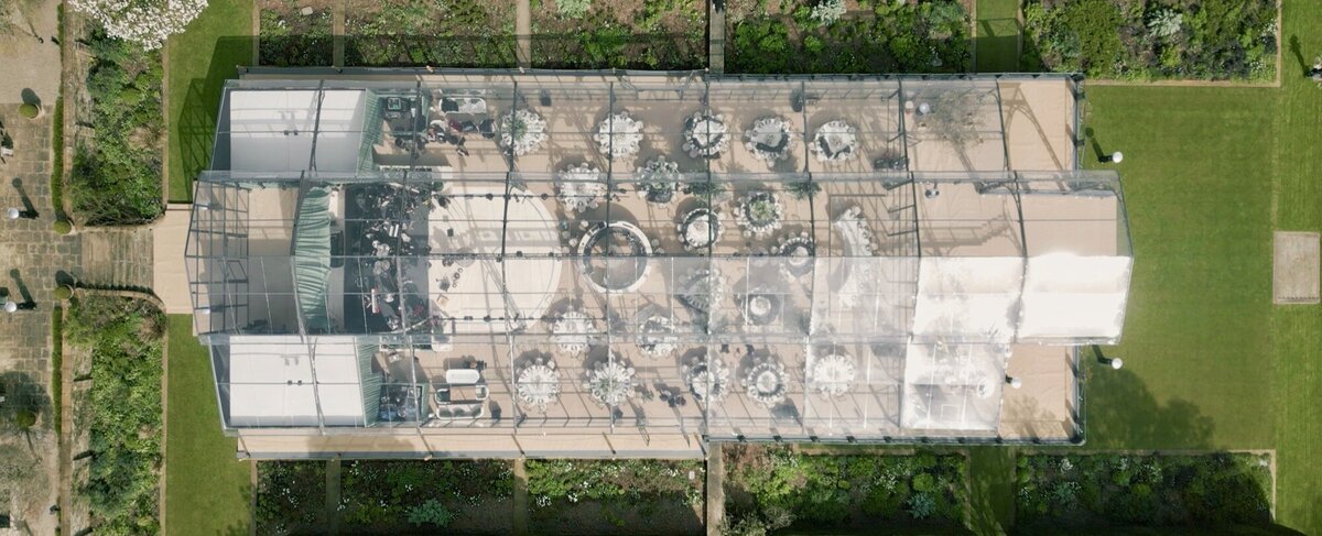An aerial view of a glass marquee on a lawn with a long walkway and flowers at the entrance for Amelia and Olly Murs