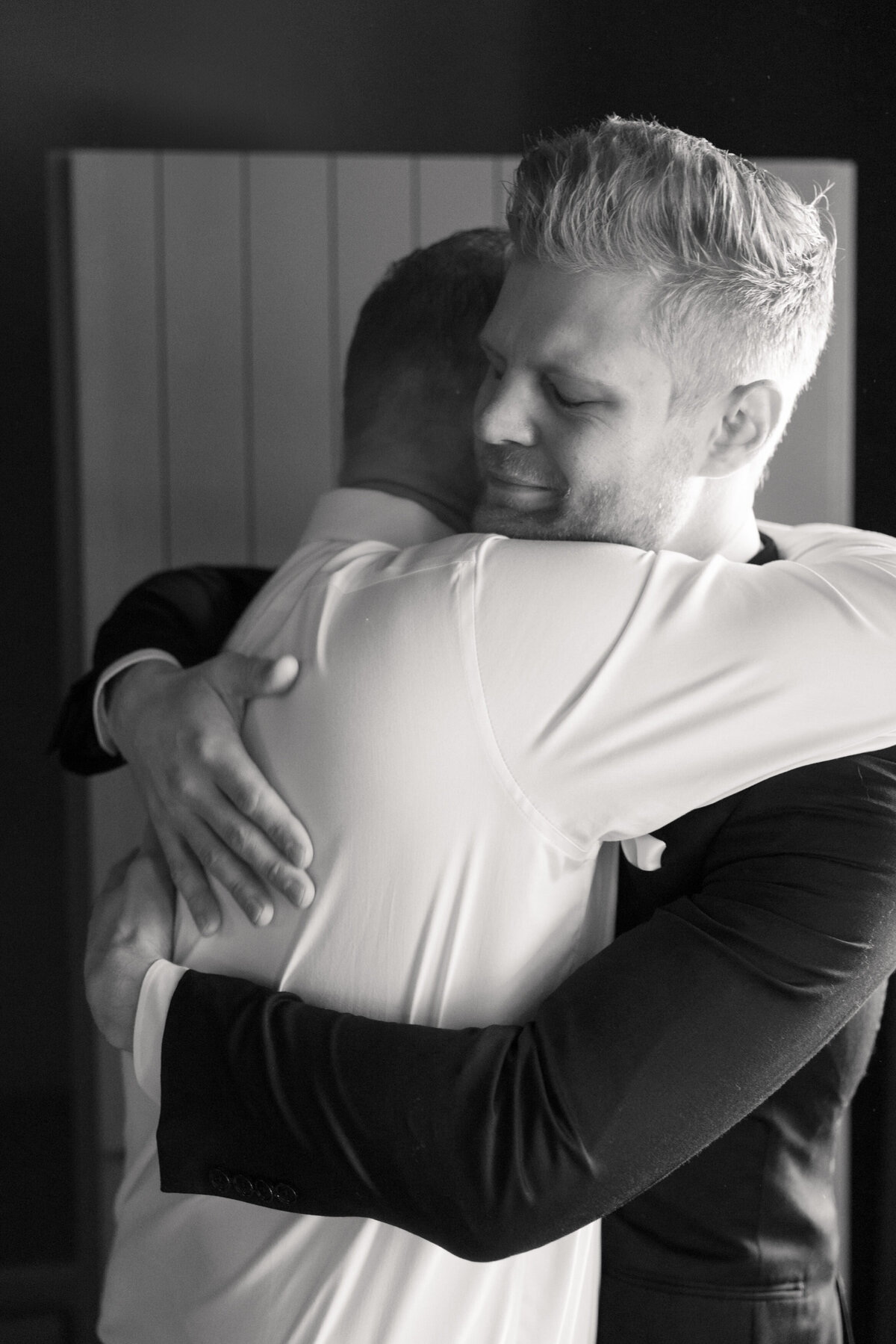 Groom hugs groomsman in emotional black and white moment, photographed in Dayton by a Philadelphia wedding photographer.