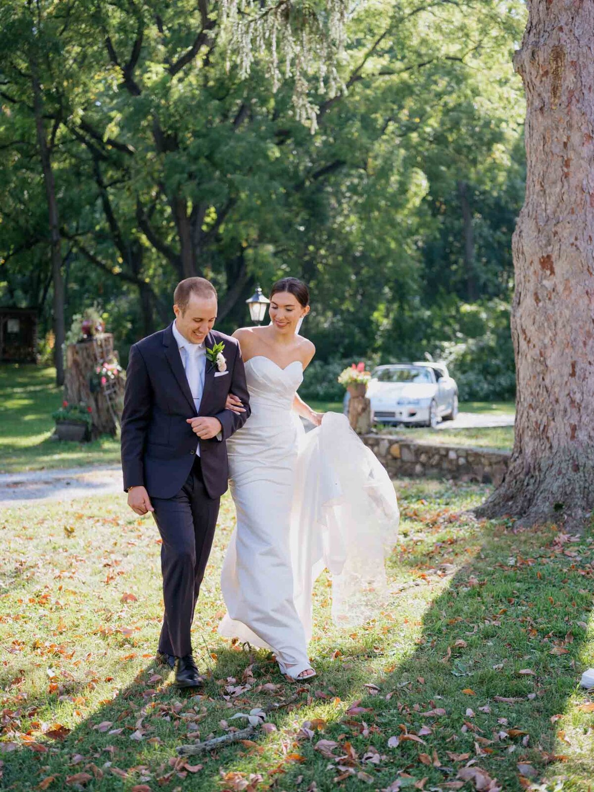Bride in elegant Maggie Sottero gown walking with her groom at their tented backyard wedding