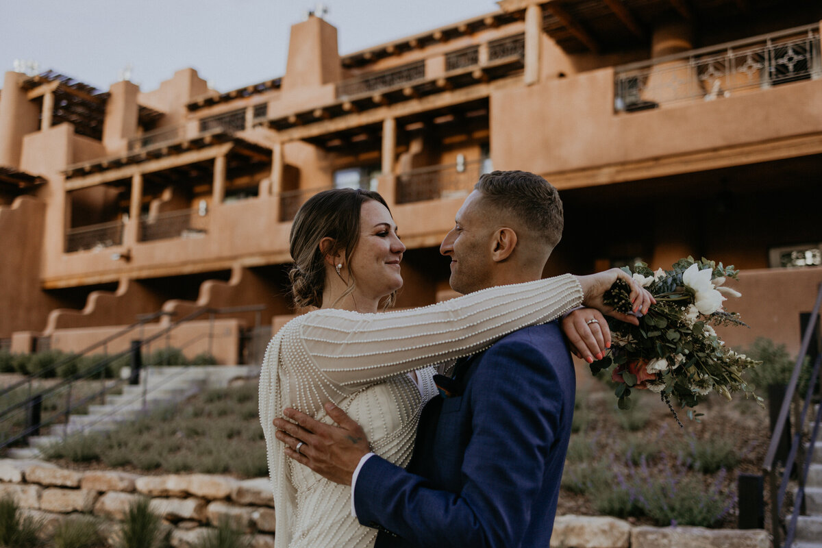 bride and groom holding each other infront of an adobe building