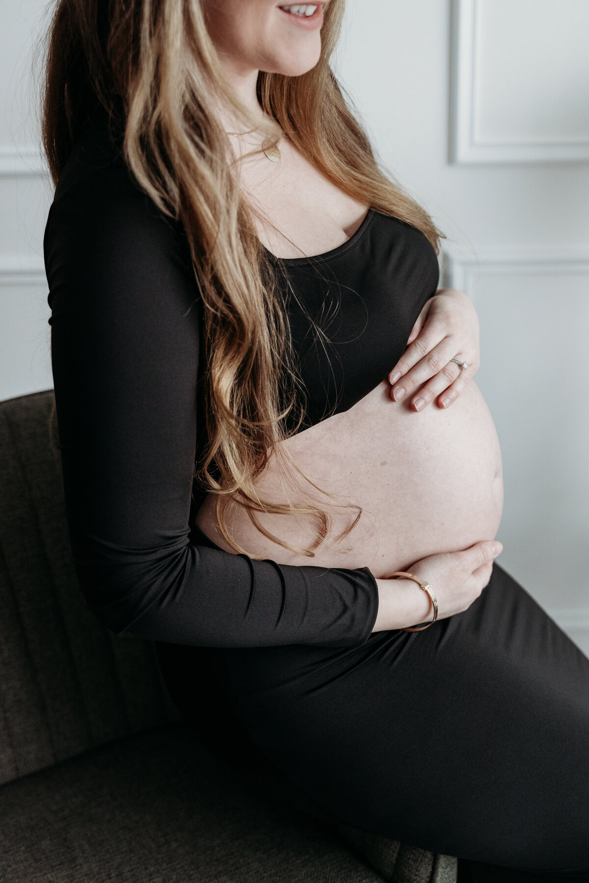 A pregnant mother in a black dress embraces her baby bump in a ligt filled studio in Bartlett, IL