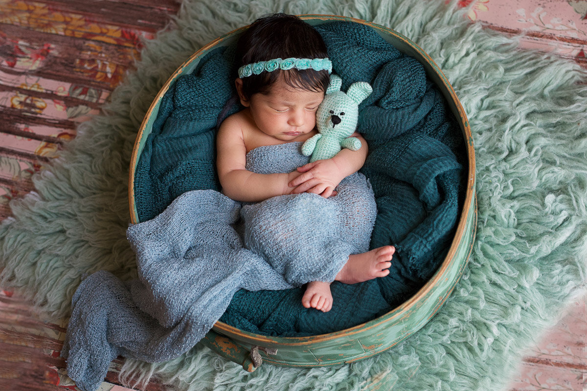 Newborn baby girl holding her knitted bear during home photo session by Yuliia Terziian photography in Calgary,Alberta.