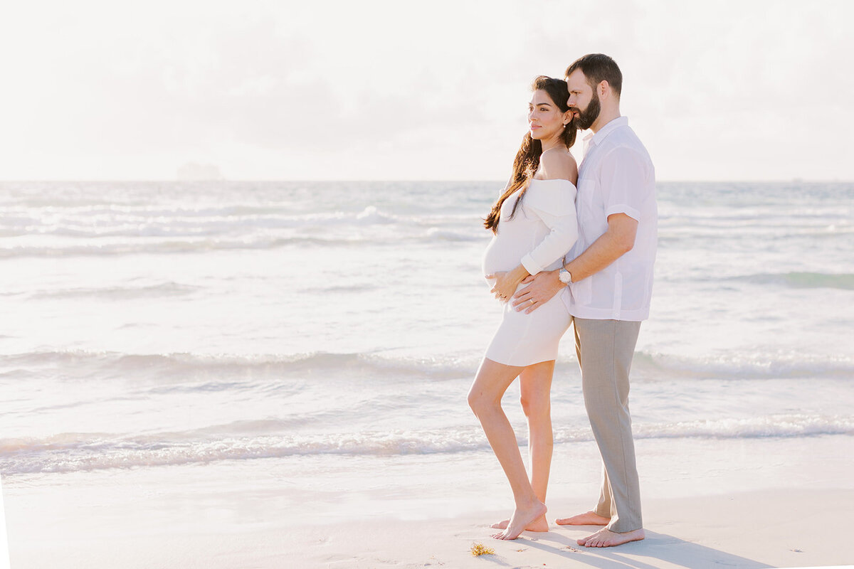 A couple embraces near the beach, celebrating the beauty of their growing family.