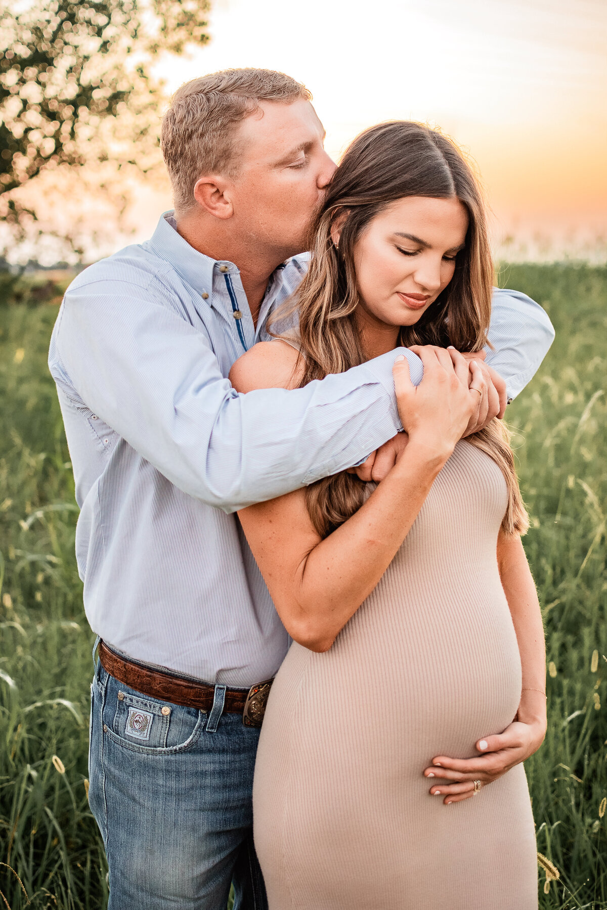 A husband hugs his wife from behind as she looks at her growing baby bump,