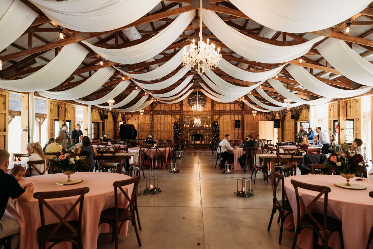 Indoor barn reception setup with draped ceiling and chandeliers