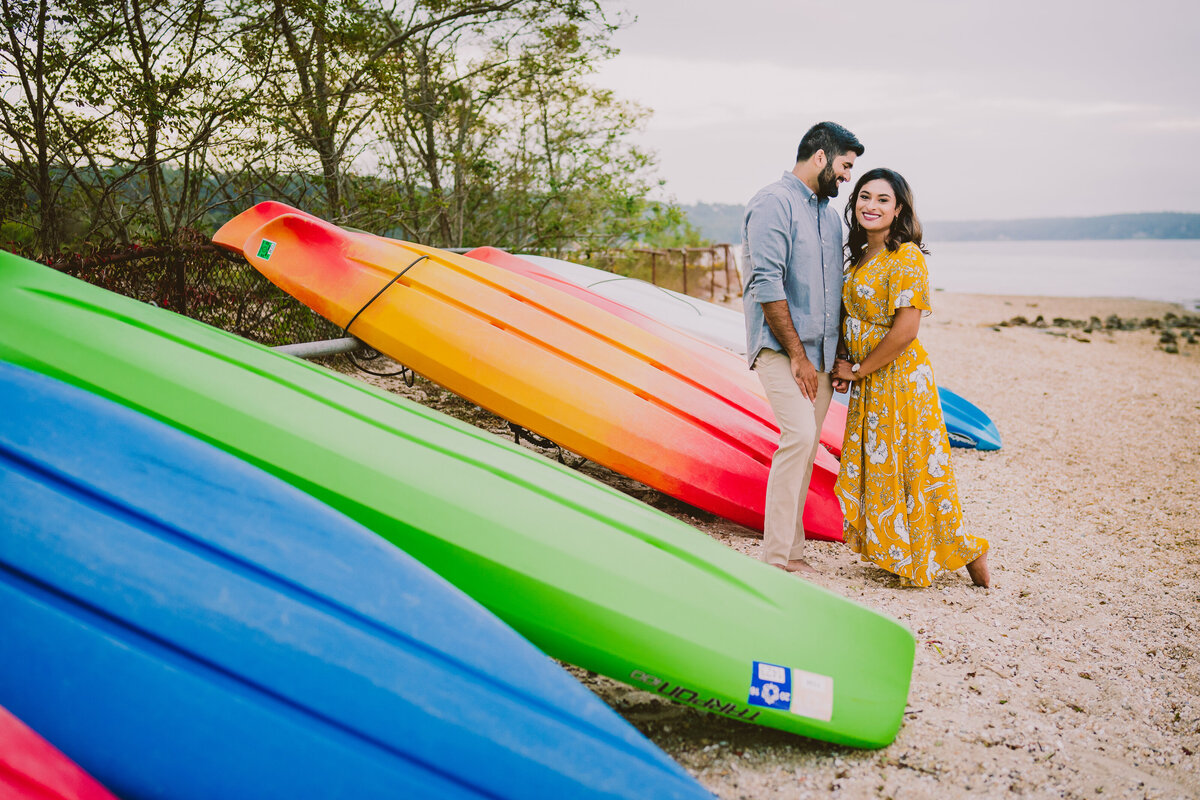 an engagement couple standing in front of colorful canoes at the lloyd neck beach in ny