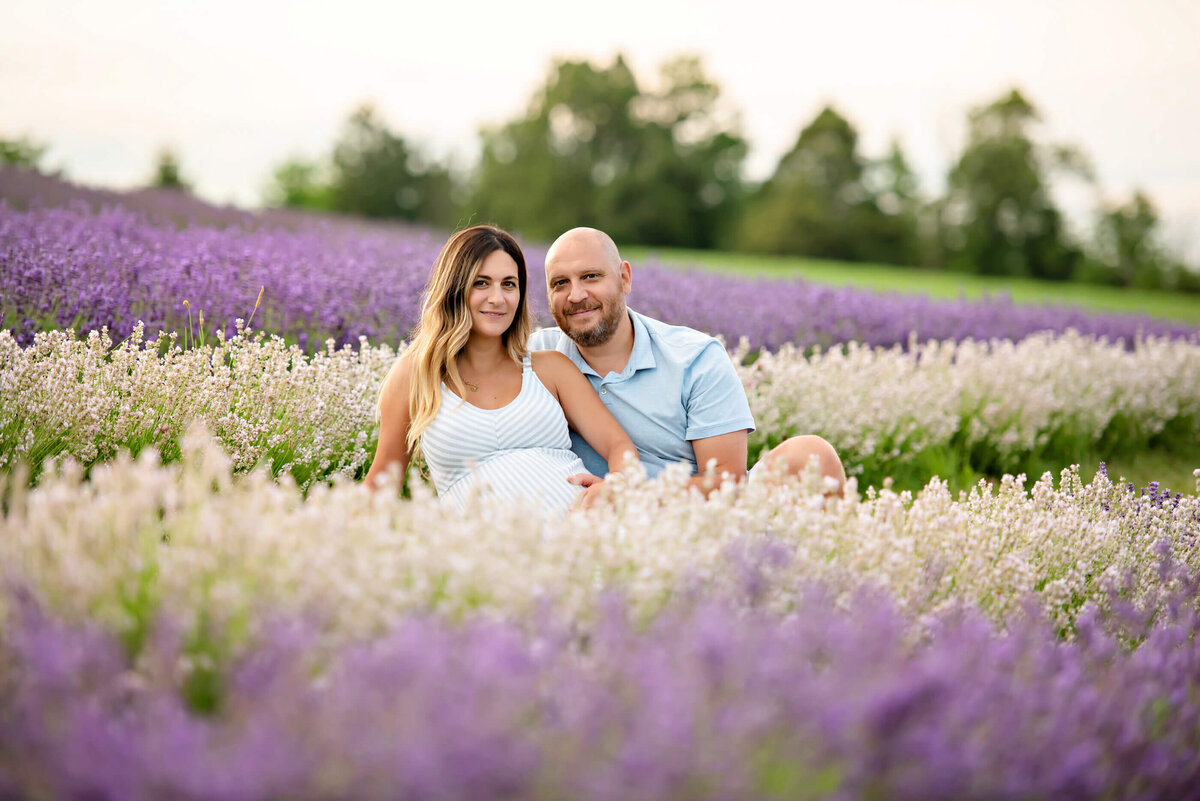 husband and wife sitting in a lavender field for their outdoor maternity photos 