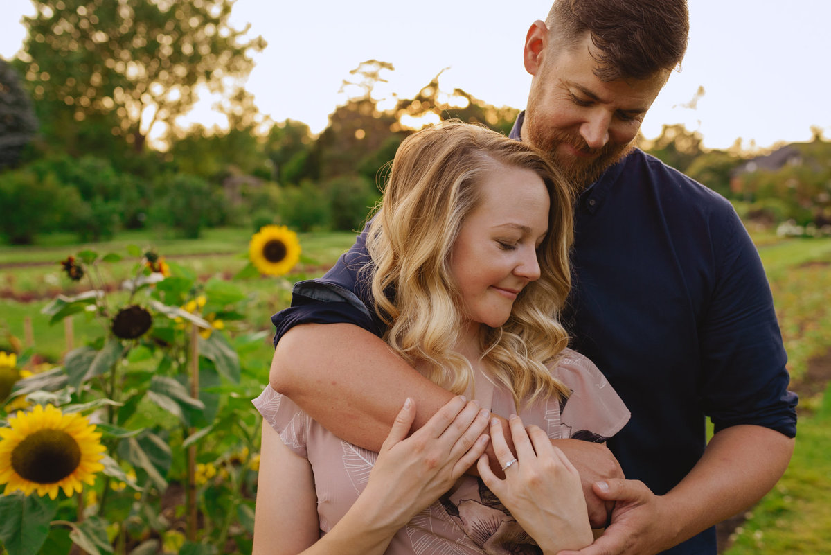 engaged couple standing in a field of sunflowers at sunset