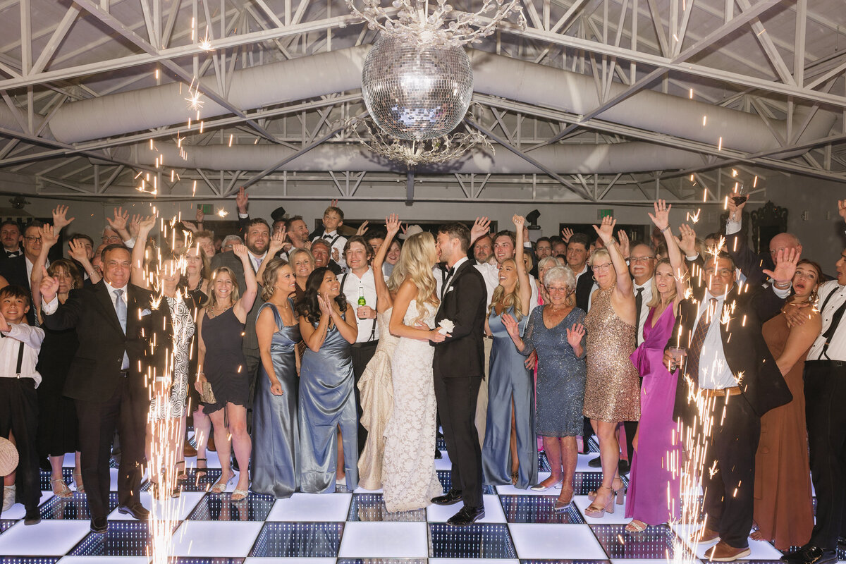 Guests cheering while bride and groom kiss with cold sparklers on dance floor